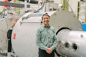 Man stands in front of large machine, smiles at camera.