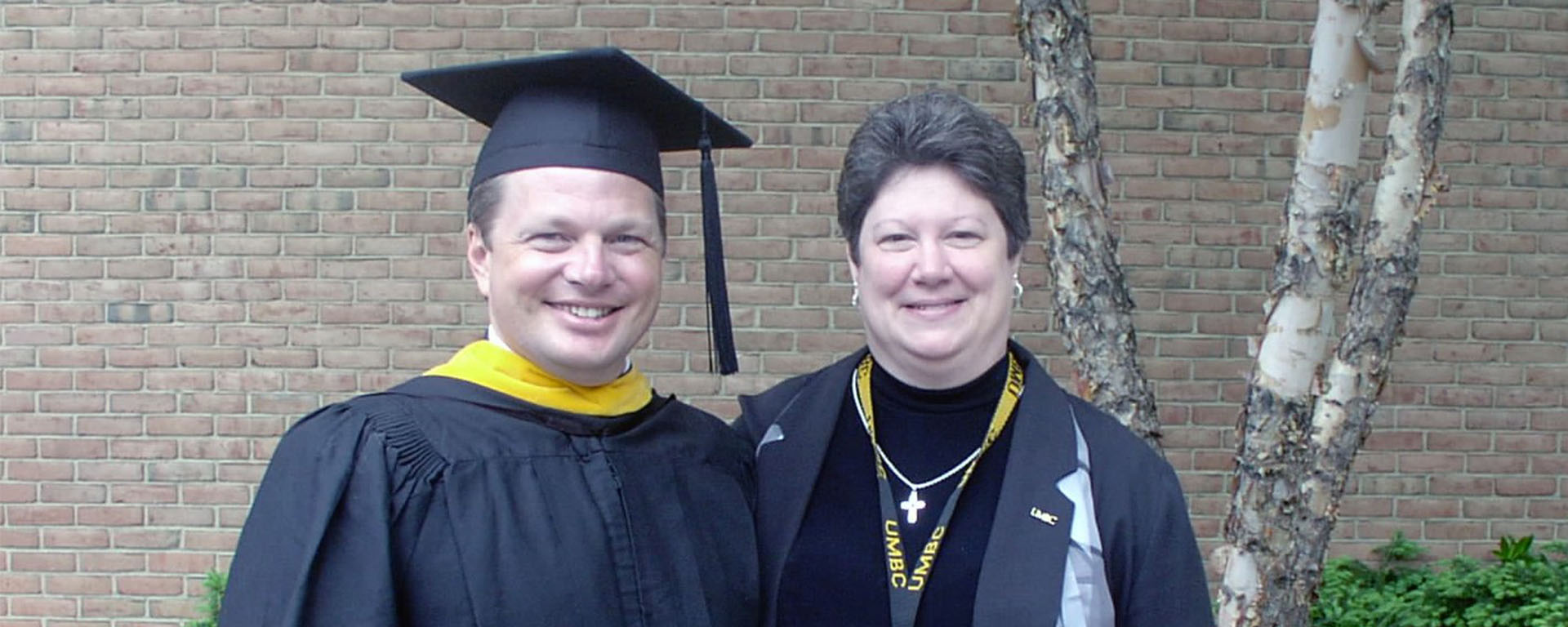 man and woman standing in front of brick building with small tree in background