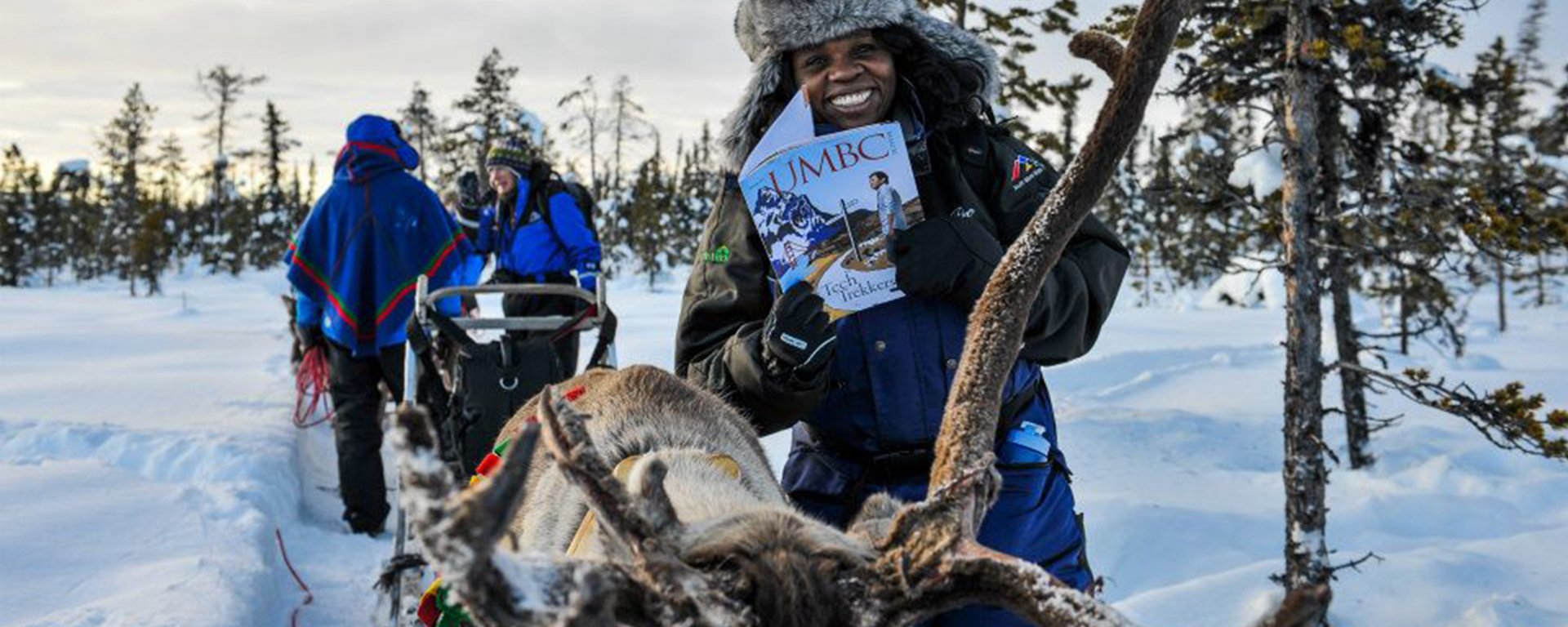 Visual storyteller Lola Akinmade Åkerström holding an issue of UMBC Magazine in the snow next to a dog sled.