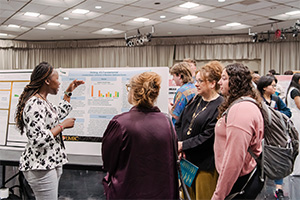 People standing near a poster board presenting research at UMBC's 2024 Undergraduate Research and Creative Achievement Day in 2024.
