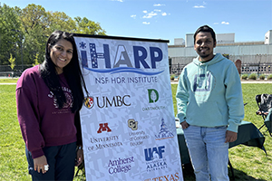 Two people stand outside next to a banner that reads "iHARP"
