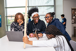 Four young people looking at computer screen and smartphone in math laboratory at UMBC