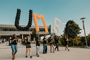 seven students marching with U-M-B-C balloon letters as a display during UMBC Convocation