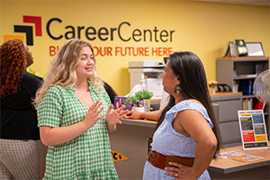 two women in discussion, standing in front of Career Center signage