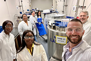 people in white coats stand in a lab with metal tanks in the background