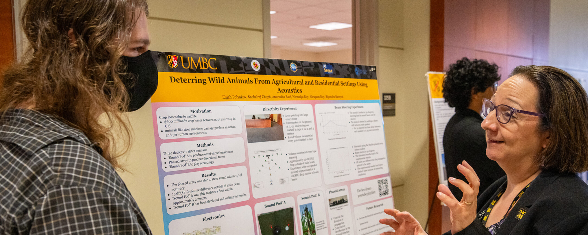 two people discuss poster presentation with U-M-B-C- logo