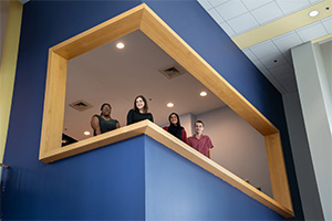 Four Fulbright college students stand together inside a building on a blue balcony