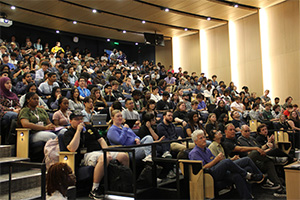 A lecture hall filled with hundreds of people in tiered seating